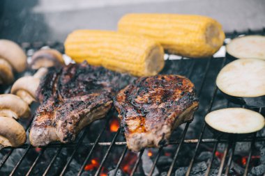 selective focus of tasty steaks grilling on bbq grid with mushrooms, corn and sliced eggplant clipart