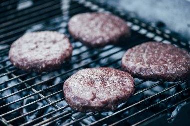 uncooked fresh burger cutlets grilling on bbq grid clipart
