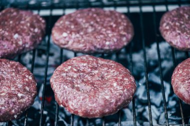 close up of uncooked fresh burger cutlets grilling on bbq grid clipart