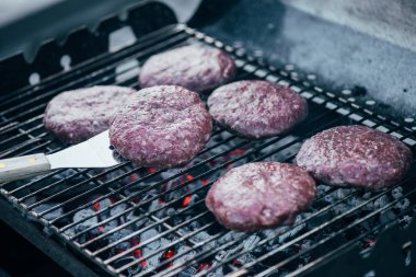 selective focus of spatula and uncooked fresh burger cutlets grilling on bbq grid clipart
