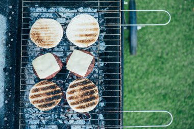 top view of delicious fresh burgers ingredients grilling on barbecue grid clipart