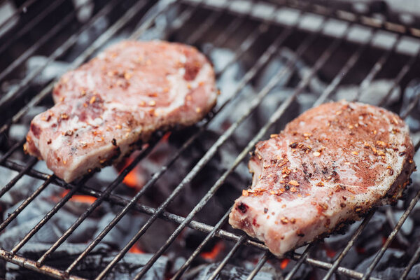 selective focus of juicy raw steaks grilling on barbecue grid with smoke