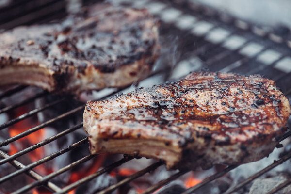 selective focus of juicy spicy steaks grilling on barbecue grid with smoke