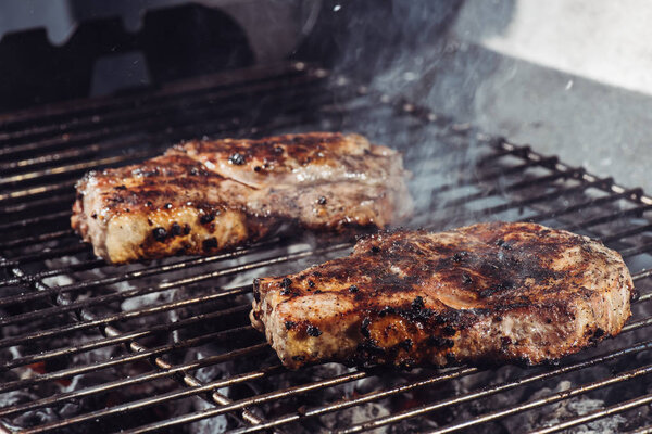 selective focus of juicy tasty steaks grilling on barbecue grill grade with smoke