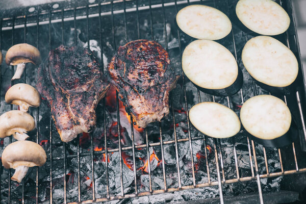 juicy tasty steaks grilling on hot coals with mushrooms and sliced eggplant