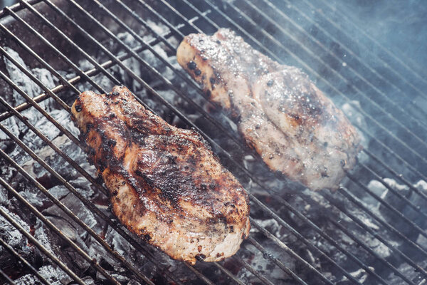 selective focus of juicy steaks grilling on hot coals with smoke