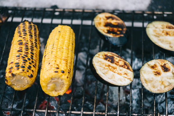 selective focus of yellow corn with crust and eggplant slices grilling on barbecue grid