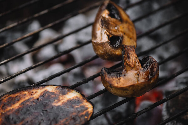close up of mushrooms and eggplant slice grilling on barbecue grid