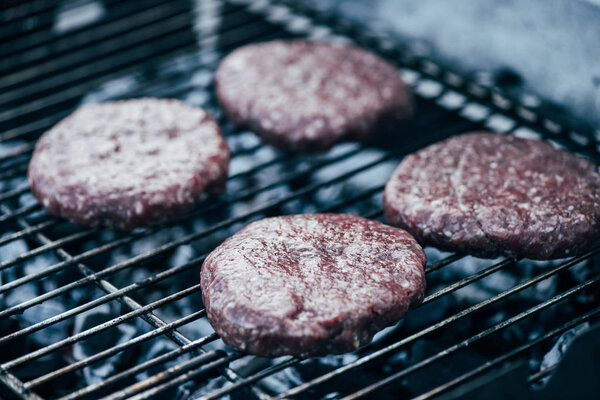 uncooked fresh burger cutlets grilling on bbq grid