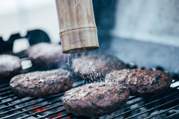 selective focus of salt falling from salt mill on tasty grilled bbq burger cutlets
