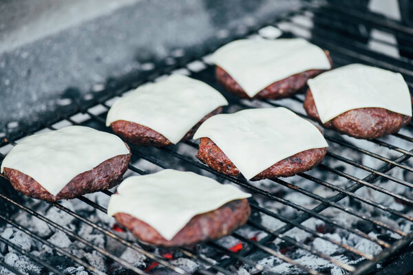 selective focus of fresh burger cutlets with cheese grilling on bbq grid