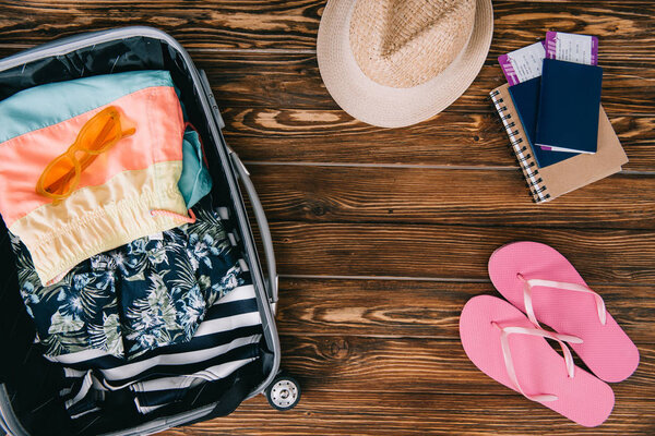 top view of passports with tickets and summer clothes in travel bag on wooden surface