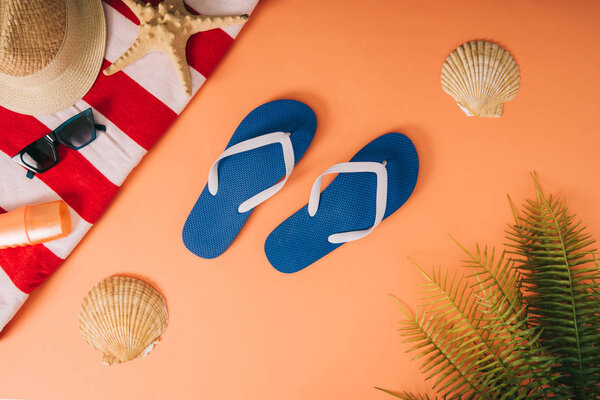 top view of summer accessories and sunscreen on orange background with palm leaves and seashells