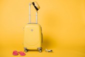 világos sárga utazótáska, szalmakalap, pink flip papucs és repülőgép modell a sárga háttér