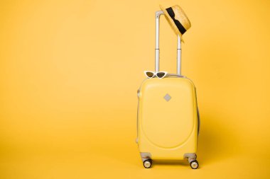 bright yellow suitcase, sunglasses and straw hat on yellow background