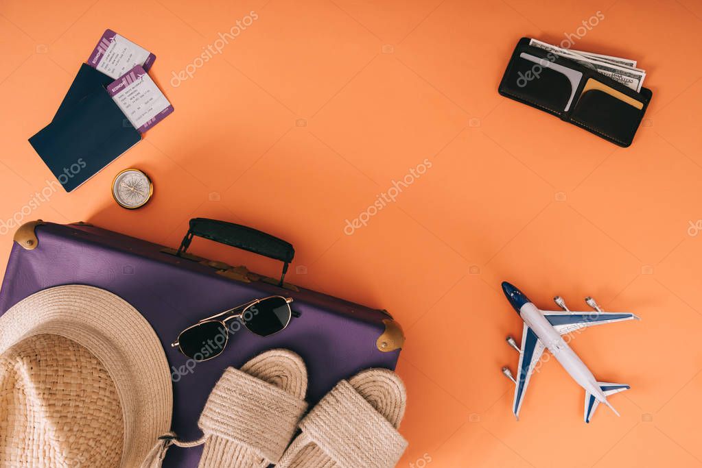 top view of summer accessories on travel bag, plane model, wallet and passports with tickets on orange background