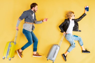 Stylish couple with suitcases and tickets running on yellow background clipart