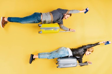 Funny couple lying on suitcases and holding tickets on yellow background clipart