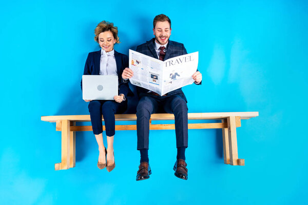 Well-dressed couple reading newspapers and smiling on blue background