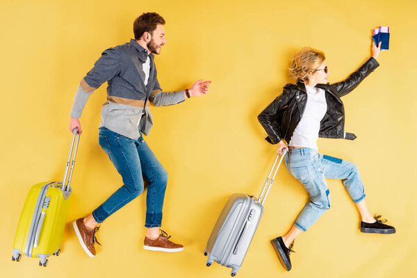 Stylish couple with suitcases and tickets running on yellow background