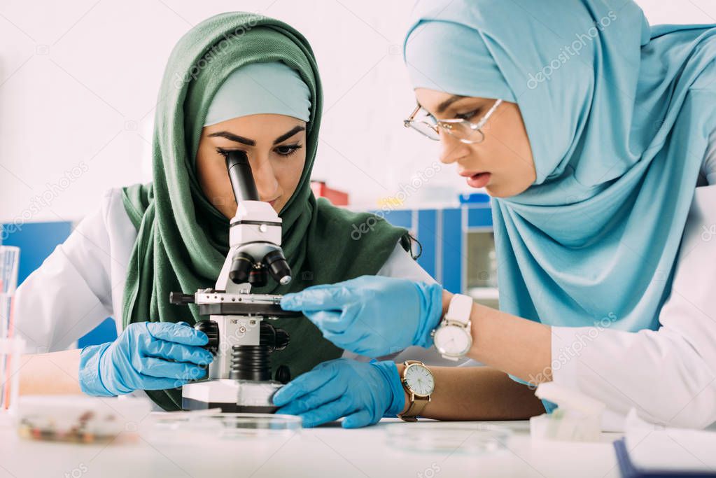 focused female muslim scientists in hijab using microscope during experiment in chemical laboratory