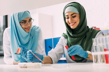 kimyasal laboratuvar deneyi sırasında kadın Müslüman bilim adamları hijab tüp ve pipet ile gülümseyen