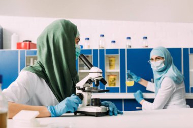 deneme sırasında kimyasal laboratuvar arka planda çalıştığı meslektaşı ile mikroskop kullanarak kadın Müslüman bilim adamı