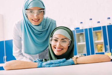 koruyucu gözlük ve laboratuvar kamerada bakarak hijab mutlu Müslüman kimyagerler