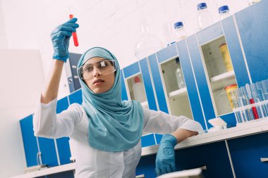 kadın Müslüman bilim adamı laboratuvarda test tüpü kırmızı sıvı ile tutarak gözlük