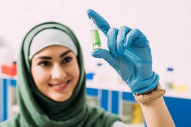 cam ampül laboratuvarda tutan gülümseyen kadın Müslüman bilim adamı