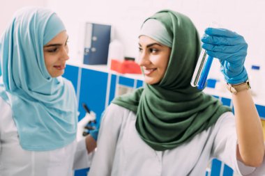cam test tüpleri reaktifleri ile deneme sırasında kimyasal laboratuarda tutan gülümseyen kadın Müslüman bilim adamları