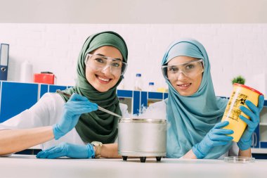 kadın Müslüman bilim adamları kuru buzun içinde kimyasal laboratuvar ile deneme yaparken kameraya bakarak gözlük