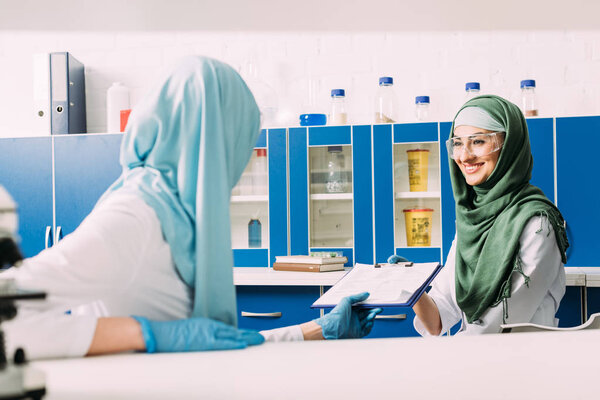 female muslim scientists in hijab holding clipboard during experiment in chemical laboratory