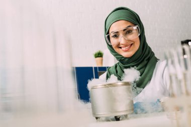 Kuru buz laboratuvar ile deneme sırasında kameraya bakarak gülümseyen kadın Müslüman bilim adamı