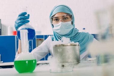 Kuru buzun içinde kimyasal laboratuvar deney sırasında şişesi tutan kadın Müslüman bilim adamı