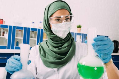 kimyasal laboratuvar deney sırasında şişeler tutan kadın Müslüman bilim adamı