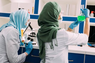 arkadan görünüşü şişesi tutarak ve kimyasal laboratuvar deney sırasında mikroskop kullanarak kadın Müslüman bilim adamları