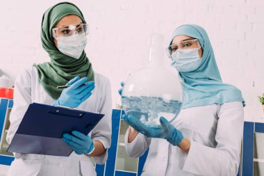 Pano ve şişesi holding tıbbi maskeli kadın Müslüman bilim adamları konsantre wth sıvı kimyasal laboratuvar