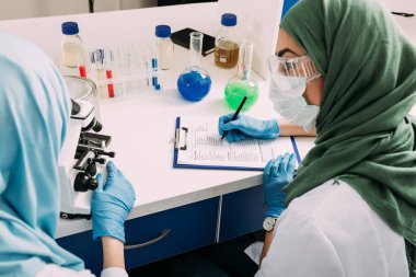 mikroskop kullanma ve kimyasal laboratuvar deney sırasında Pano'da yazma kadın Müslüman bilim adamları