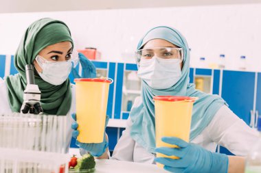 Klinik atık kapları tutarak ve kimyasal laboratuvar kamerada bakarak kadın Müslüman bilim adamları