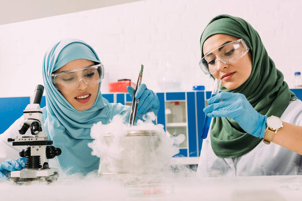 мусульманские ученые в хиджабе экспериментируют с микроскопом и сухим льдом в химической лаборатории
