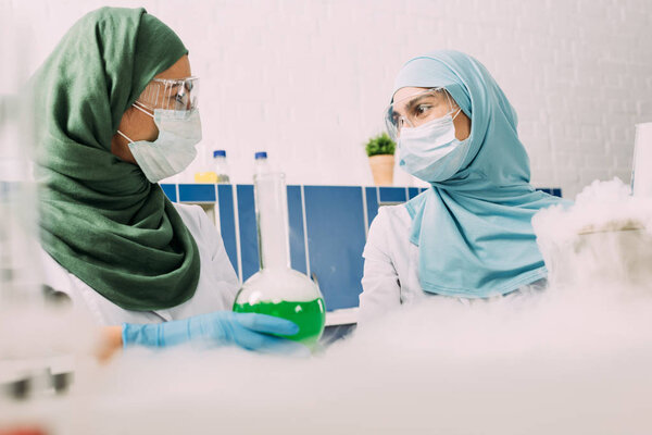 мусульманские ученые с фляжкой, смотрящие друг на друга во время экспериментов с сухим льдом в химической лаборатории
