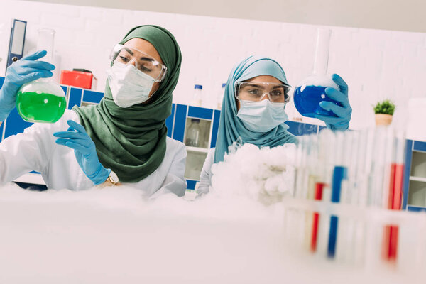 мусульманские ученые в медицинских масках держат фляжки во время экспериментов с сухим льдом в химической лаборатории
