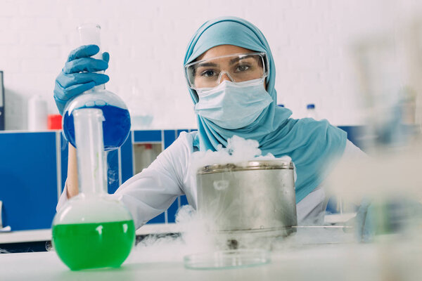 мусульманская ученая держит фляжку во время эксперимента с сухим льдом в химической лаборатории

