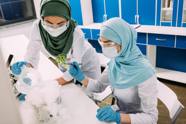 женщины-ученые-мусульмане экспериментируют с сухим льдом и брокколи в химической лаборатории
