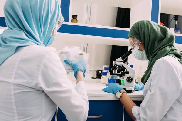 женщины-ученые-мусульмане экспериментируют с сухим льдом и используют микроскоп в химической лаборатории
