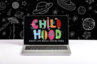 laptop on table with enjoy life while you are young and childhood lettering on screen with white space illustration on black  clipart