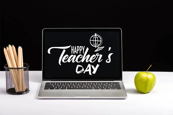 新鲜的绿色苹果 彩色铅笔和笔记本电脑在桌子上与愉快的老师天文字和地球在屏幕上查出在黑色 — 图库照片