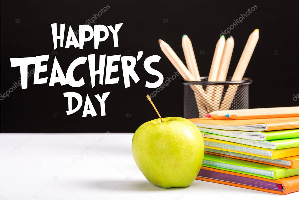 fresh apple, notebooks and color pencils on table with happy teachers day  lettering on black 