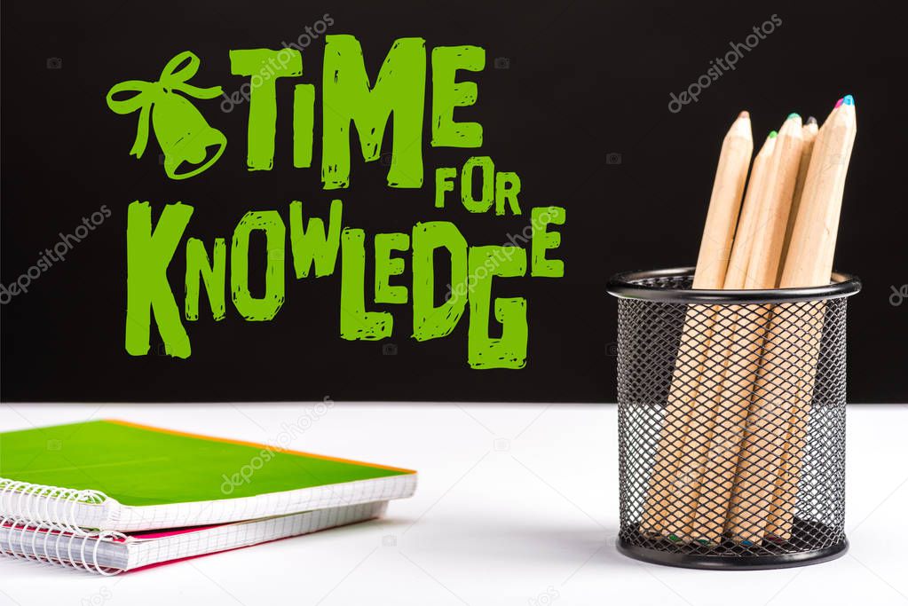 notebooks and color pencils on table with green time for knowledge lettering and bell sign on black 